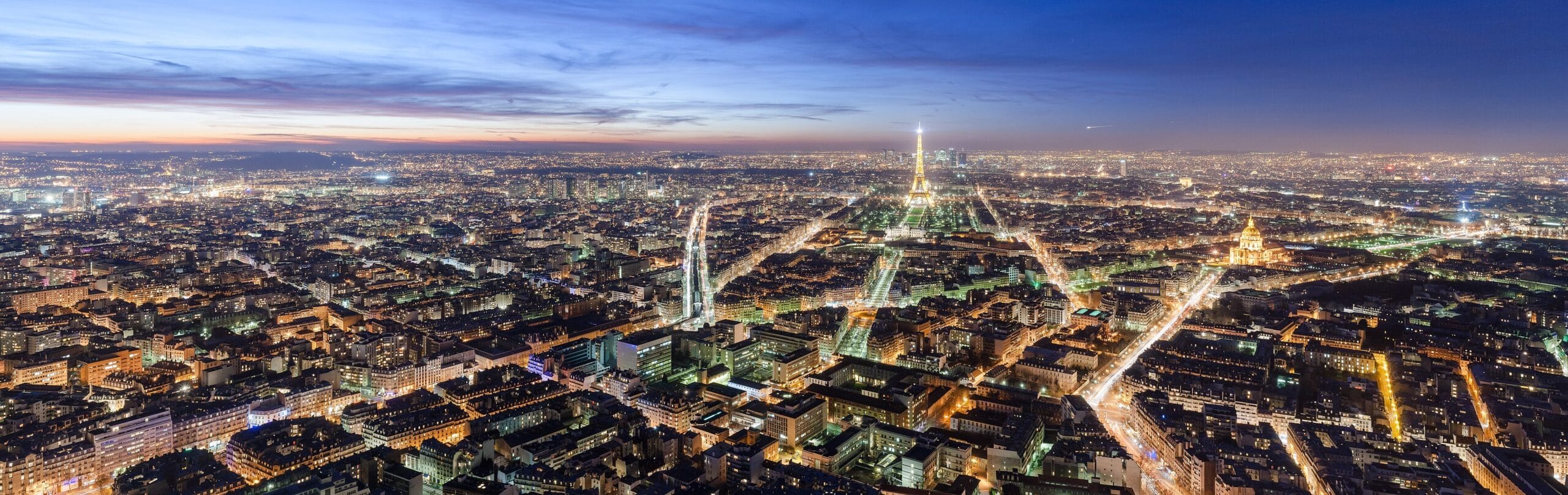 Paris skyline at night with the Eiffel Tower lit up, seen across the city rooftops